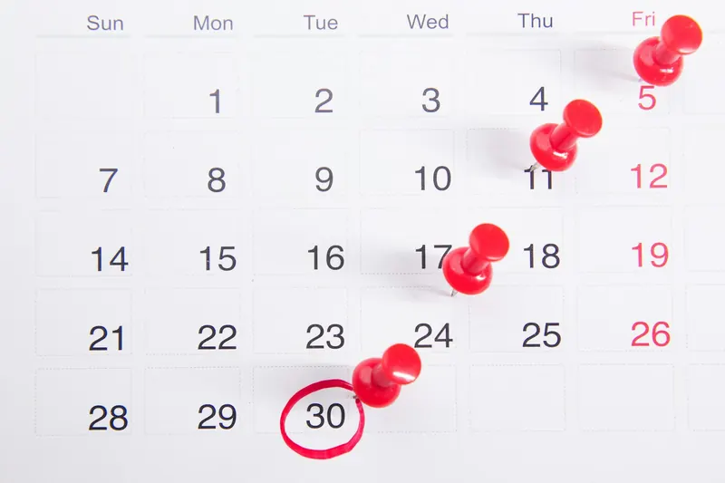 Monthly paper calendar with red push pins on several days and the 30th circled in red