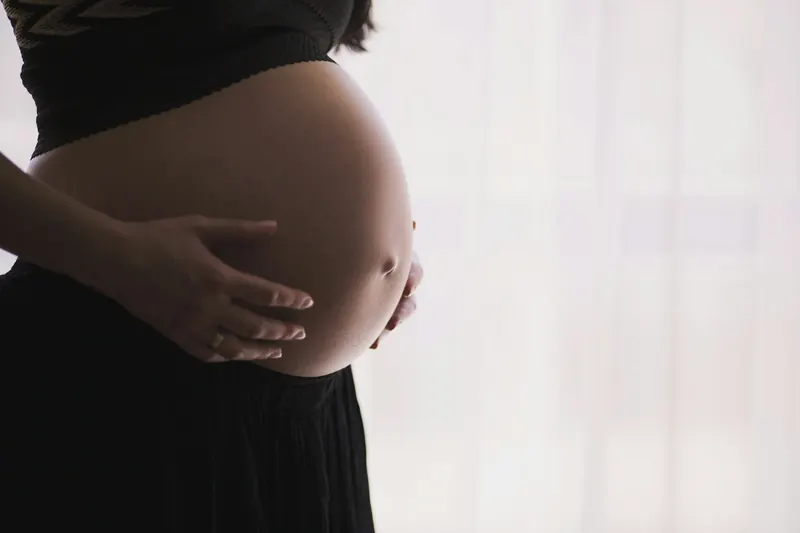 Side view of a pregnant woman holding her belly in front of a bright window